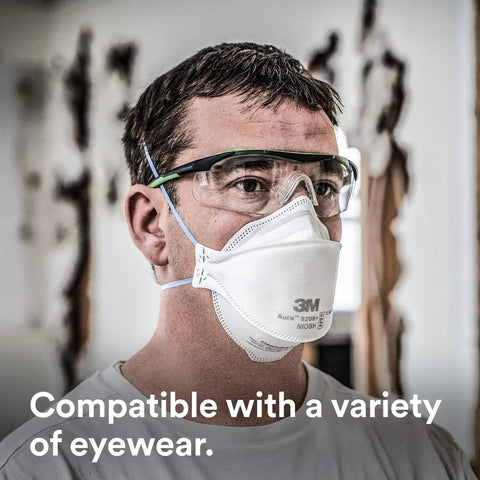 Man wearing Super Comfy N95 Particulate Respirator Pack Of 20 With 3 Panel Flat Fold Design For Easy Facial Movement Reduces Eyewear Fogging Disposable Individually Wrapped Comfortable NIOSH Approved For Smoke And Dust, with safety glasses, in a workshop.