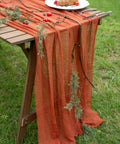 Rustic Fall Thanksgiving Table Runner Terracotta Cheesecloth Weave 120 Inches Long Hand Dyed Soft Cotton Gauze on a wooden table with greenery.