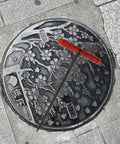 Heavy Duty Steel Manhole Cover Opener With Solid T Handle Grip Rust Resistant Multi Purpose Pull Lifter Hook For Sewer Lid Snagging And Jobsite Hauls No Sweat Tradesman Gear above a decorative manhole cover.