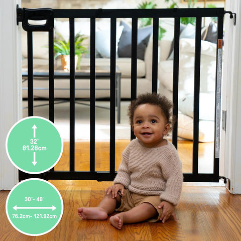 Child sitting in front of Deluxe Stair Gate For Pets And Kids, Super Easy Install No Fuss Secure Build, Fits Openings 30 To 48 Inches Wide, 32 Inches Tall, black wood.