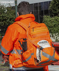 Worker wearing Hi Vis Orange Safety Backpack With Reflective Panels, Adjustable Hard Hat Holder, and utility pockets on site