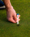 Hand placing Premium Slick Rubberized Golf Tees With Durable Plastic Base For Low Spin Launch Assorted Colors 4 Pack on grass.