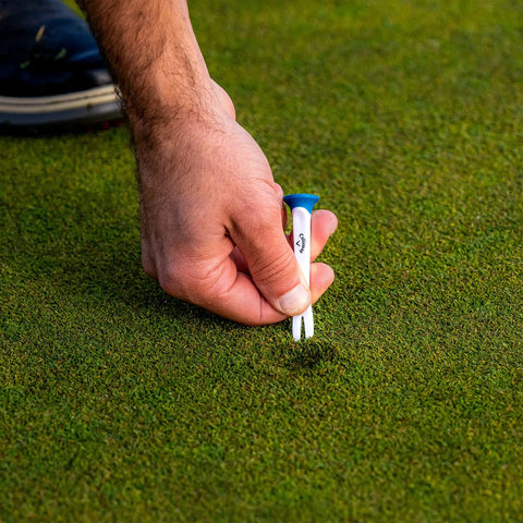 Hand placing Premium Slick Rubberized Golf Tees With Durable Plastic Base For Low Spin Launch Assorted Colors 4 Pack on grass.