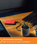 5TB Portable External Hard Drive In Red With Built In Backup Software Ransomware Defense And Password Protection USB 3.1 3.0 Ready Ultra Slim And Durable For On The Go Data Storage connected to laptop on wooden desk