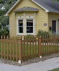 Wooden picket fence in front of a yellow house with garden, featuring decorative stars on window trims and manicured landscaping.