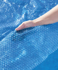 Close-up of hand holding Hella Effective 10 Foot Solar Pool Cover made of blue mesh, showing its bubble design for trapping heat.