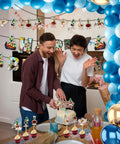 Couple celebrating with cake and Migration Theme Decor Kit with world maps, travel icons, arrows, birds, and suitcases displayed.