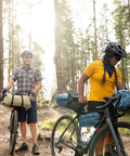 Cyclists with bikes equipped with Cabezon FB 6 Frame Bag For Bikes, 6L waterproof storage pack, reflective trim in forest trail setting.