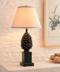 Rustic Pinecone Accent Table Lamp In Aged Bronze Finish, 29 Inch Tall With A 15 Inch Tapered Shade on a living room table