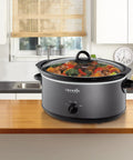 Huge 7 Quart Manual Slow Cooker Serving As A Real Weeknight Hero With Removable Stoneware Pot, High And Low Settings Plus Auto Warm Mode, No Fuss Dishwasher Safe Cleanup, Charcoal Finish on a kitchen counter with vegetables.