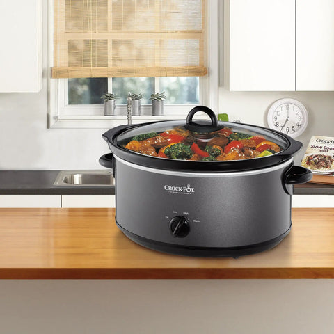 Huge 7 Quart Manual Slow Cooker Serving As A Real Weeknight Hero With Removable Stoneware Pot, High And Low Settings Plus Auto Warm Mode, No Fuss Dishwasher Safe Cleanup, Charcoal Finish on a kitchen counter with vegetables.