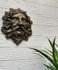 Top Tier Green Man Wall Decor, Slick 9.75 Inch Heavy Duty Cast Iron Plaque, Solid Bronze Finish mounted on textured wall.