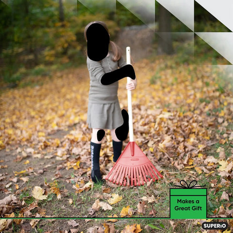 Child using a red kids rake with hardwood handle in a yard with autumn leaves