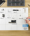 Hand using dry-erase marker on Magnetic Project Mat And Screw Organizer Pad For Electronics Repair with phone parts.
