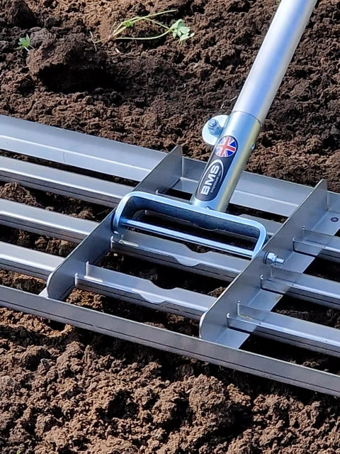 38 Inch Wide Leveling Lawn Rake With Stainless Steel Head And 72 Inch Aluminum Handle in use on soil, close-up of metal head and shaft