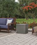 22 Gallon Outdoor Storage Box With Seat In Stone Gray Resin on a patio surrounded by wicker furniture and trees