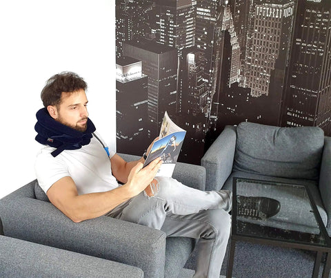 Man using Neck Traction Device For Home Pain Relief With Inflatable Cervical Stretcher Collar sitting on couch reading magazine