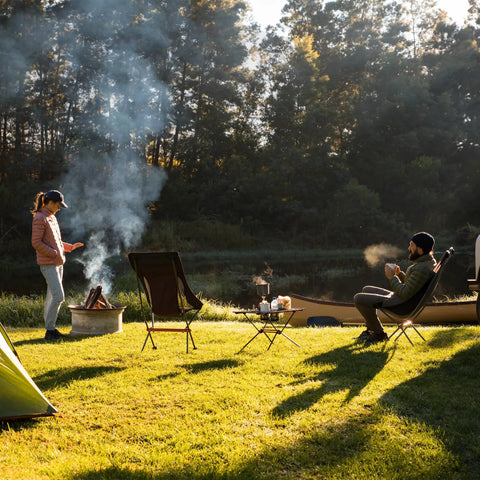 Ultralight Camping Table With Cup Holder And Carry Bag, Foldable Aluminum Backpacking Table at a campsite near a river with trees.