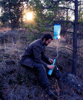 Gravity Water Filter Portable Purifier With 3L Bag And Tree Strap For Camping Hiking Emergency Prep BPA Free Survival Gear Ready Clean Water Anywhere On The Go in use, attached to a tree branch at sunset.