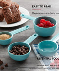 Aqua Sky Measuring Cups Set Of Four With One Quarter, One Third, One Half, And One Cup Sizes, Easy Read Markings In Standard And Metric, Nesting Design With Ring For Compact Drawer Storage, Dishwasher Safe Kitchen Essential displaying accurate measurements next to baked goods and ingredients on a kitchen table.
