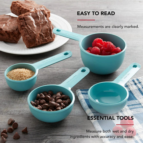 Aqua Sky Measuring Cups Set Of Four With One Quarter, One Third, One Half, And One Cup Sizes, Easy Read Markings In Standard And Metric, Nesting Design With Ring For Compact Drawer Storage, Dishwasher Safe Kitchen Essential displaying accurate measurements next to baked goods and ingredients on a kitchen table.