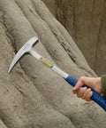 Rock Pick Hammer 22 Oz USA Made Geology Tool With Pointed Tip And Shock Reduction Grip held against a rock face