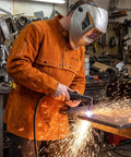 Person wearing Leather Welding Jacket With Open Back And Bib Apron Cape Sleeves in a workshop, using a welding tool, sparks flying