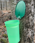 Top Shelf Maple Syrup Bucket Kit includes a green food-grade sugar container hanging on a tree for sap collection.
