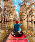 Person paddling a red canoe through a narrow, tree-lined waterway with moss hanging from branches.