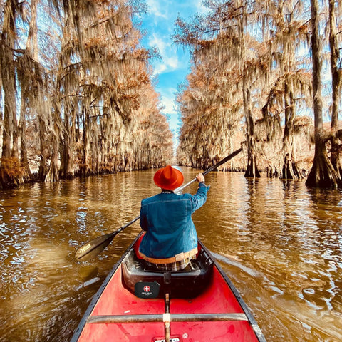 Person paddling a red canoe through a narrow, tree-lined waterway with moss hanging from branches.