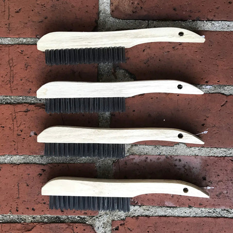 Four-Piece Shoe-Handle Wire Scratch Brush Set With Black Oil-Tempered Steel Bristles on brick background