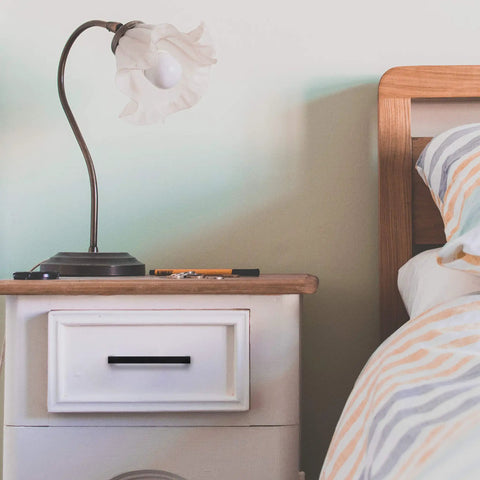 Bedroom nightstand with 60 Pack Sleek Matte Black Square Cabinet Handle and decorative lamp beside bed with striped bedding.
