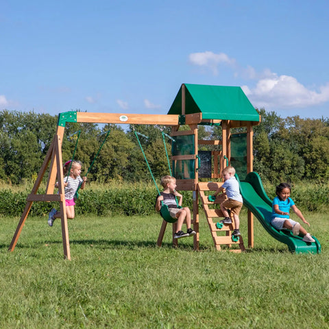 Children playing on Buckley Hill Cedar Wood Swing Set With Wave Slide, Elevated Play Deck, Rock Wall Ladder, Belt Swings, Canopy Roof.