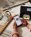 Selphy CP1500 Wireless Photo Printer In Black Ultra Portable Mini Printer With WiFi and Smartphone Connectivity on desk with scrapbook.