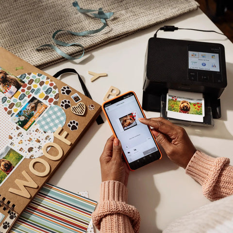 Selphy CP1500 Wireless Photo Printer In Black Ultra Portable Mini Printer With WiFi and Smartphone Connectivity on desk with scrapbook.