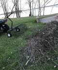 Pine Straw Rake and Lawn Sweeper 60 Inch Wide Steel Leaf Collector Attachment connected to ATV near cleared debris pile