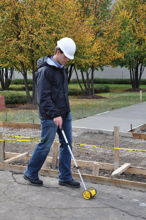 Engineer using Dual 4-Inch Measuring Wheel RT204 Distance Measurer on construction site, yellow wheel visible, telescoping handle