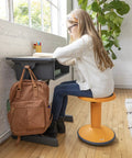 Child seated on SitWell Wobble Stool With Adjustable Height For Active Seating In Classrooms And Home Learning, orange