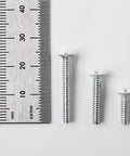Three assorted size screws from 75 Pack Wall Plate Screws Set With Slotted Oval Heads For Outlets And Light Switches, next to a ruler.