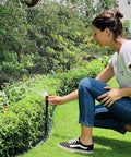 Woman adjusting a Flexible Multi-Adjustable Above Ground Garden Sprinkler System in a vibrant garden with adjustable heads and hose.