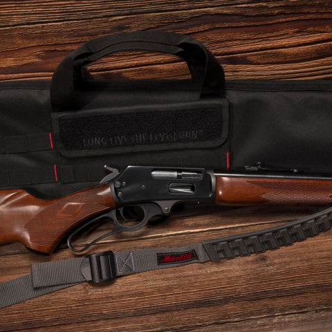 Baktrak Traction Web Rifle Sling With 36 Inch Length 500 Pound Rated Swivels Slim Non Slip Pad next to rifle and gun bag.