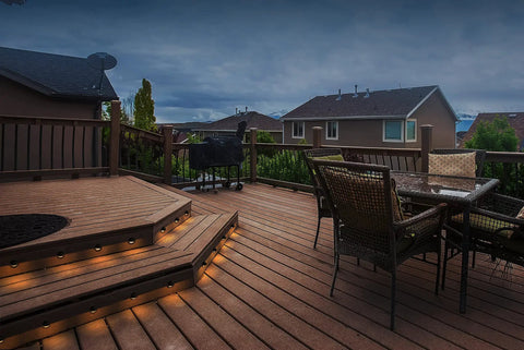 8 Pack Low Voltage LED Deck Lights Mini Eyelid Step Lights illuminating wooden deck steps and patio at dusk