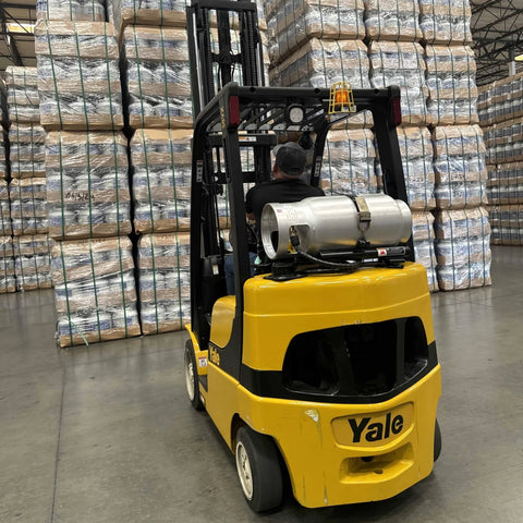 Aluminum 33.5 lb forklift propane tank with gauge mounted on back of yellow Yale forklift in warehouse.