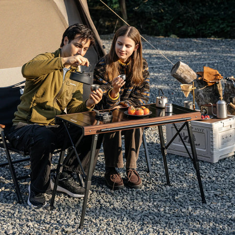 Height Adjustable IGT Camping Table With Detachable Edge Mount For Extra Storage in outdoor setting with two people cooking.