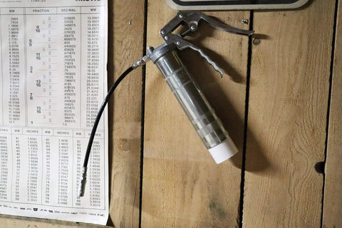 One Hand Pistol Grip Grease Gun Kit with zinc barrel and 500mm hose hanging on wall with industrial chart in background