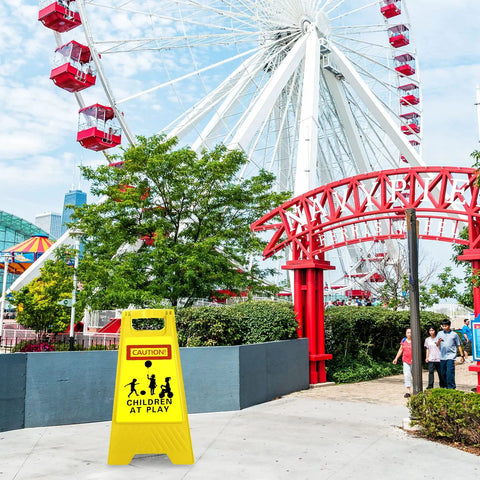 Four Pack 24 Inch Slow Down Kids At Play Sign Reflective Double Sided Street Safety Signs With Portable Handles For Neighborhoods Yards Schools And Parks Yellow in front of a ferris wheel.