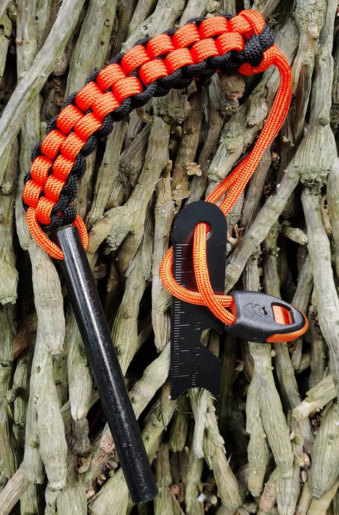 Drilled Ferro Rod Fire Starter Kit with 4 Inch Flint Steel, paracord lanyard handle, striker and whistle on a wooden background.