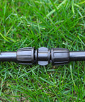 Ten Pack Half Inch Drip Irrigation Barbed Coupling Connectors installed on black tubing lying on grass