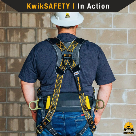 Solid As A Rock Full Body Fall Protection Safety Harness With Cushioned Lumbar Pad Multiple D Ring Attachment Points Quick Lock Buckles ANSI OSHA Certified Job Site Ready Work Gear With Durable Tool Loops And Phone Pocket worn by a worker in a gray shirt and white hard hat