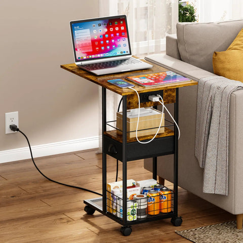 C Shaped Side Table With Charging Station And Wheels For Bedroom Living Room And Home Office Type C USB Ports And Two AC Outlets To Charge Up To Four Devices Plug And Play placed beside a sofa with a laptop and tablet on top.